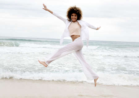 beautiful girl with afro hair and white dress jump on the beachの写真素材