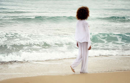 beautiful girl with afro hair and white dress walk by the sea