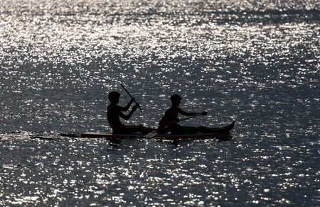 Silhouette of two men kayaking on the sea at sunset