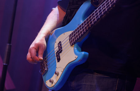 Guitarist playing on a blue bass guitar during a concert.の写真素材