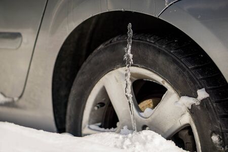 Winter driving problems, snow and ice. Extreme winter series. Huge icicles on the dirty car wheel. Dangerous ice build up car wheel.  Frozen car wheel in ice and snow. Close up of car tire on the snowy road.の写真素材