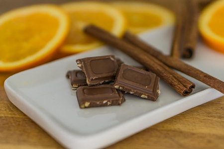 Closeup of pieces of milk chocolate with crushed, roasted almonds, cinnamon sticks and fresh, crisp defokus orange.の写真素材