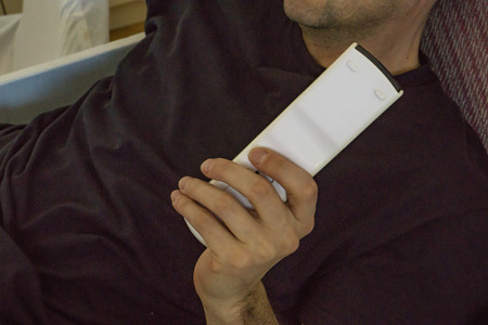 A young man sitting on the couch to rest with a remote control in hand.