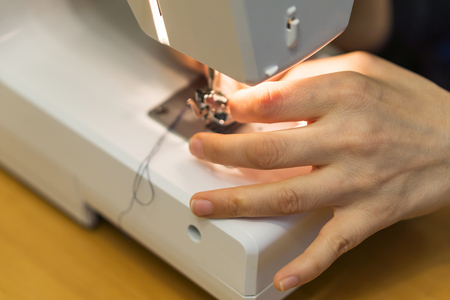 Closeup of hand a young woman spends thread a sewing machine at home.の写真素材