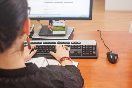 Business environment, defocused young woman working on a keyboard, monitor and mouse with cable.の写真素材