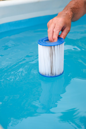 Replacement Pool Filter Cartridge in Hand on a Blue Pool Background. Filter Reuse.の写真素材