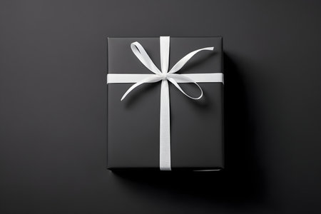 Black gift box with white ribbon on black background. Top view.の素材