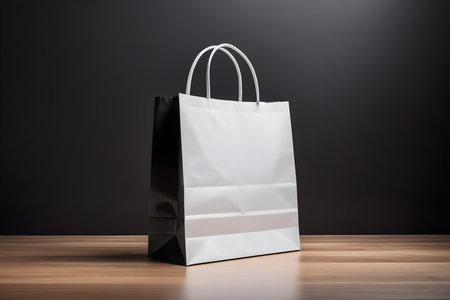 Black and white paper shopping bags on wooden table over dark background.の素材