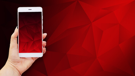 Mockup image of hands holding white mobile phone with red screen on polygonal backgroundの写真素材