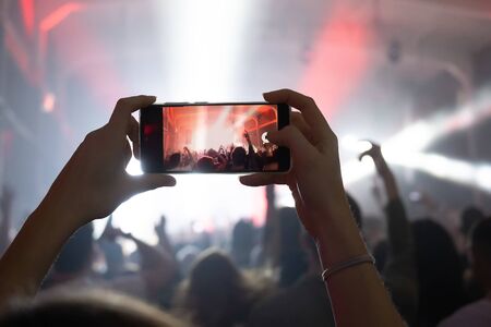 girl hands at a concert shoots videos and photos of the crowd and stage on a smartphone. music festival in the club. joyful momentsの写真素材
