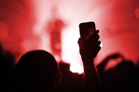 smartphone in the hand of a fan shooting a video for memory at a concert of a favorite group. The atmosphere of a music festival with a red stage.の写真素材