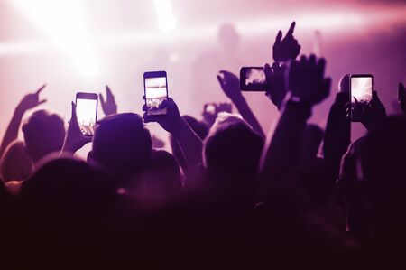 people from the crowd at a music festival in front of the stage are shooting videos and photos on their smartphones. The atmosphere of popular concerts. poster for show advertisingの写真素材