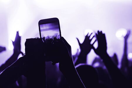 hands from the crowd with a can shoot video on a smartphone as a keepsake of a music festival. blurred background. atmosphere of a musical concertの写真素材