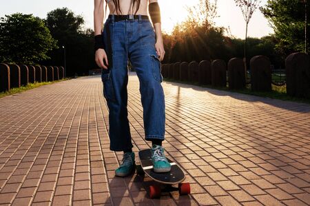 slender girl with dreadlocks in jeans and a top rides a longboard at sunset. beautiful teenager girl...