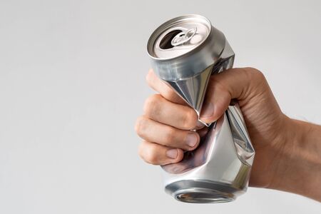 male hand squeezes an empty aluminum can for recycling. expression of anger and powerlessness. metallic packaging for drinksの写真素材