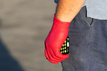 male hand in a red disposable glove holds a smartphone. protection against the spread of coronavirus. public placeの写真素材