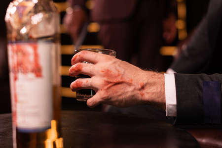 A man with a glass of whiskey and blood in his hands in an expensive suit. Alcoholism and Domestic Violenceの写真素材