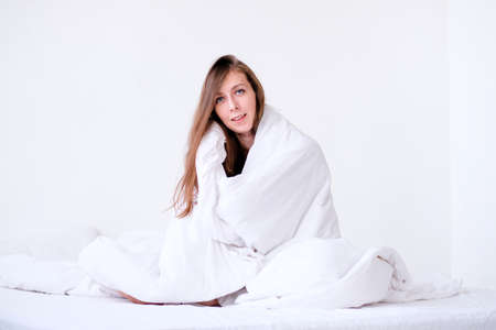 girl in a white blanket. bed rest at home. white linens. bask under the covers. overslept for work. the girl got sick. heating seasonの写真素材