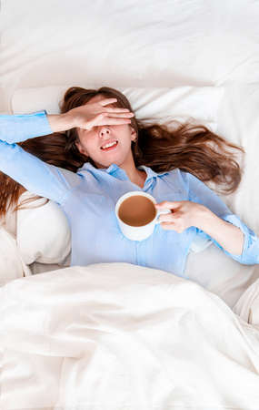 young woman lies in bed with a cup of coffee. sweat mode. a cup of coffee in bed. morning vigor. Morning coffeeの写真素材