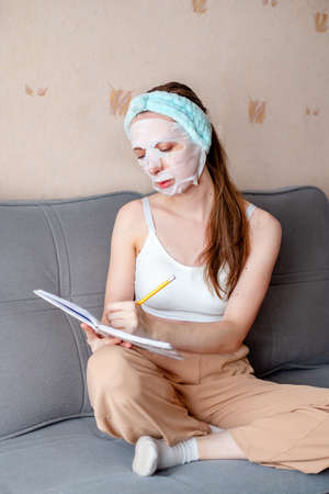 girl in a cosmetic mask sits at home and writes in a notebook. home treatments for the face. freelancer at work. tkneya msk for the face. work from homeの写真素材