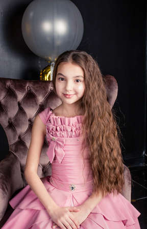 girl with long hair sits on a chair. Girl in a pink fluffy dress. photo session in the studio.の写真素材