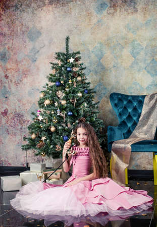 girl with christmas tree. girl with long hair sits on a chair. Girl in a pink fluffy dress. Christmas photo session in the studio. call the old phoneの写真素材