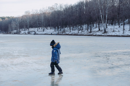 Little boy on big ice. Frozen lake near the forest. Winter landscape of frozen ice. A boy walks on frozen ice. Ice skatingの写真素材