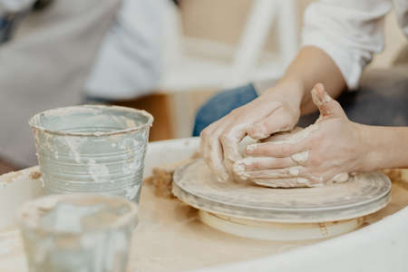 modeling on a potter's wheel. Hands are molded from clay. Creative workshop. The girl sculpts from...