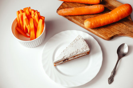 A piece of carrot cake with carrots sliced on white tableの写真素材