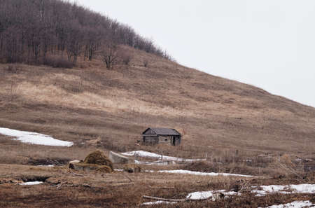 Old abandoned wooden hut on background of green hills. Gloomy weather. Grey cloudsの写真素材