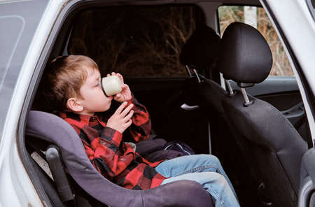 Autotrip with children. Traveling by car. Boy drinks from a cup in the carの写真素材