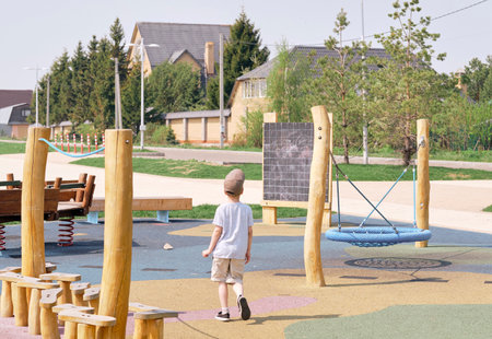 boy playing on empty playground. wooden playground in pastel colors. safe rubberized floor for...