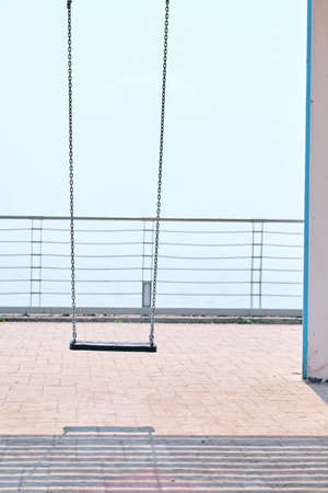 Abandoned rope swing during social isolation on a sunny day at the beach. Bright blue sky in the background. Empty swing and nobody around in a popular touristic spot. Warm summer day near the ocean.の写真素材