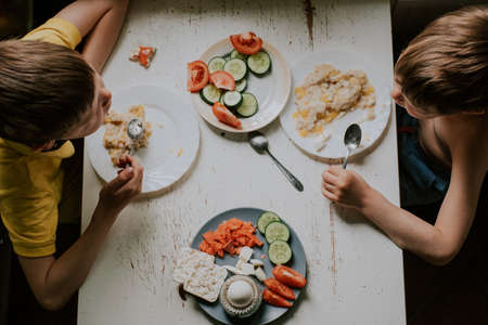 2 boys have breakfast, top view. Brothers at the table eat oatmeal and vegetablesの写真素材