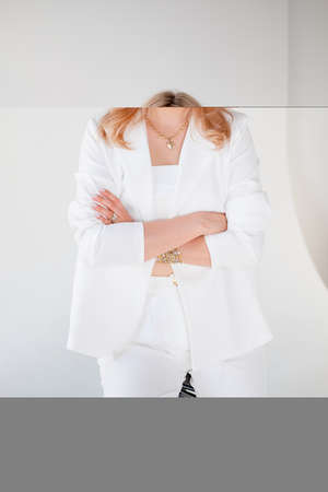 Confident young beautiful manager on white background. blonde girl in a white suit sits on a chair,...