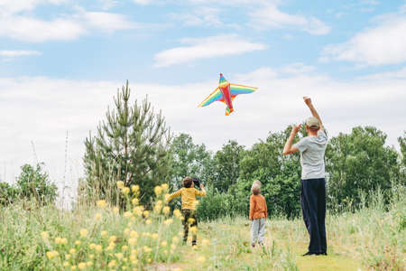 Dad and sons let a kite in the street. Happy childhood with dad. Active games on the street. A kite is high in the sky.の写真素材