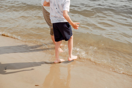 Mother and child walking on a sandy beach. Cool water in the sea. Walk along the beach barefoot.の写真素材