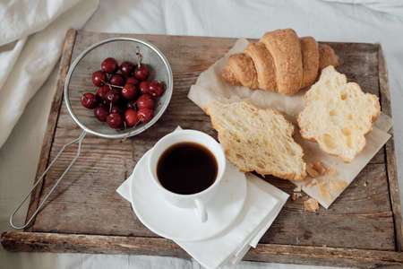 Tasty breakfast with fresh growing, coffee, cherries on a wooden tray. Hearty croissant with tomato...