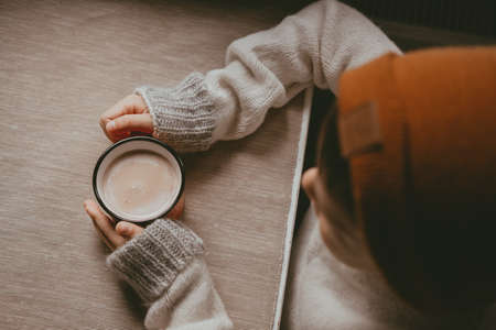 hands in a sweater hold hot cocoa, in a red mug, top view. A cozy photo with a mug in hand with copy...