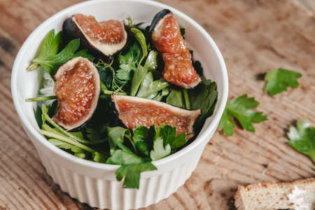 salad of fresh figs and herbs in a white bowl on a wooden background. A healthy green salad made from fresh fruits and vegetables. Proper nutrition. Cut figs into pieces. Food aestheticsの写真素材
