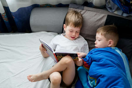 little brother reads a book on the bed for an elder. Friendship between brothers. Love for reading. Lark and owl among people. 2 boys on the bed are reading one book. Bedtime storiesの写真素材