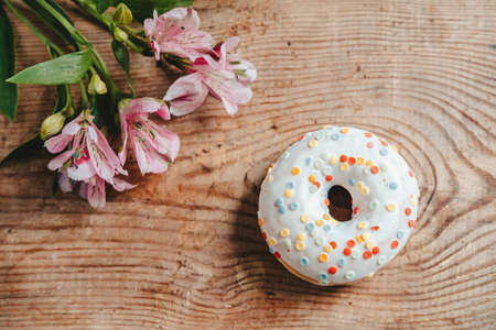 Donuts and Alstroemeria flowers on a white wooden background. View from above. donut in white glaze and candy, on a wooden table with flowers.の写真素材