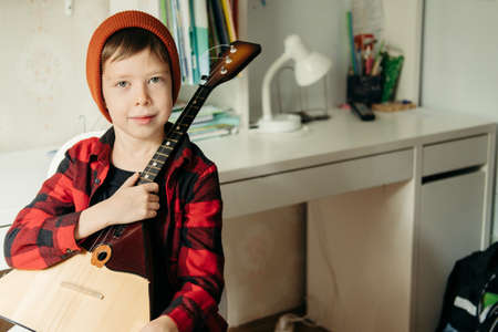 boy in a red hat and a plaid shirt plays the balalaika. Handsome boy holding his guitar. Music...