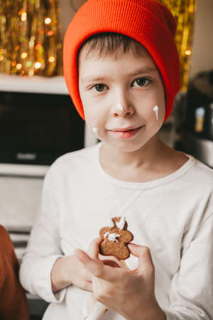 Boy decorate Christmas cookies with white icing. Children decorate a gingerbread man on a wooden...