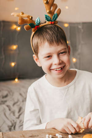 portrait of a boy in reindeer Christmas antlers on the background of an orange garland. Preparing...