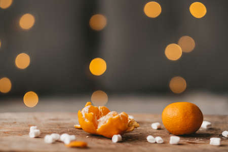 tangerines and marshmallows on a wooden table, against the background of a Christmas garland. Christmas mood. Orange fruit with marshmallows. Sweets for the new yearの写真素材