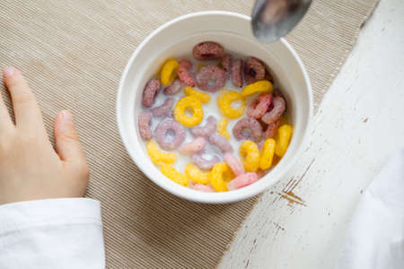 child eats colored cereals at the table, in a white kitchen. Boy's breakfast. Breakfast cereals before school.の写真素材