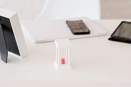 white desktop in the office, with an hourglass, against the background of a phone and a tablet