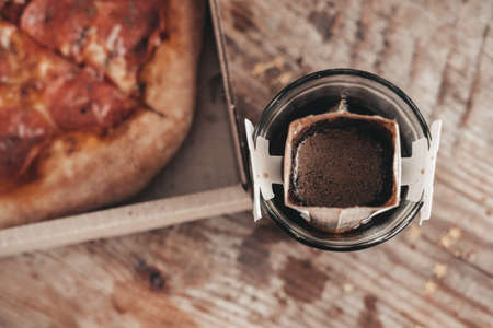 brewing coffee in a drip bag in a transparent glass, on a wooden background. Hot ground drip coffee,...