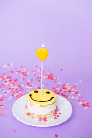 yellow cake smiley with a candle in the form of a heart on a purple background. Valentine's day and birthday conceptの写真素材